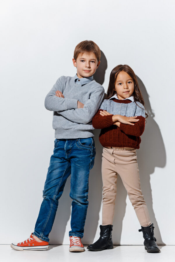 The portrait of cute little kids boy and girl in stylish jeans clothes looking at camera against white studio wall. Kids fashion and happy emotions concept